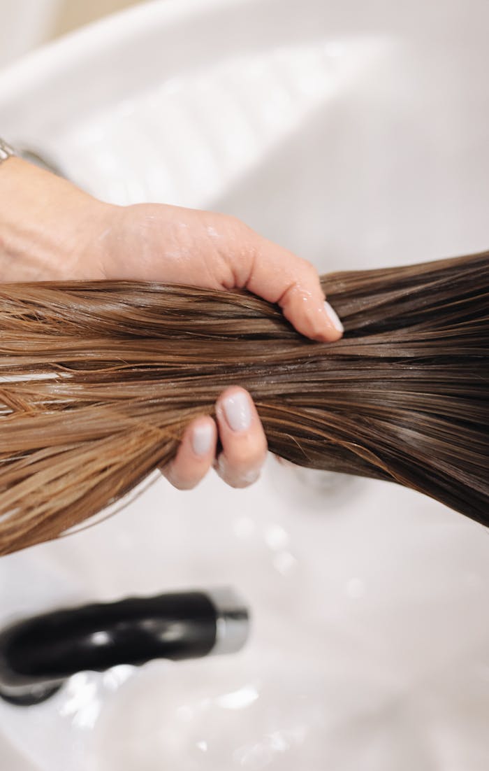 services-03 Close-up of a hand holding wet hair in a salon sink, showcasing hair treatment.