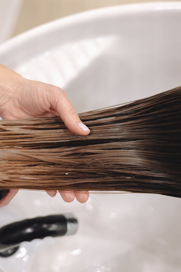 Mastering the First Impression: Your intriguing post title goes here Close-up of hand holding long, wet brown hair over a white ceramic sink, emphasizing hair care.